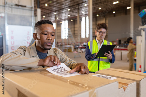 African american young man labeling cardboard box with barcode and asian manager with checklist