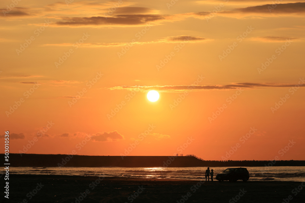 Japanese couple standing on the sandy beach of the setting sun