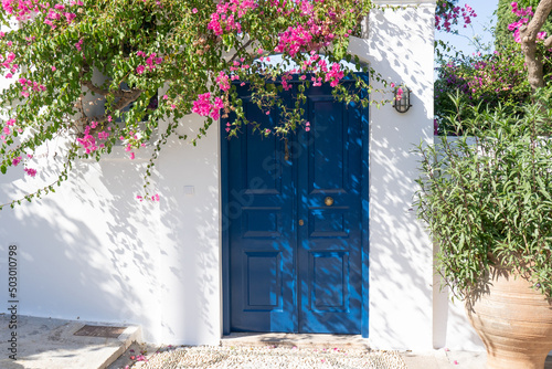 Fototapeta Naklejka Na Ścianę i Meble -  Facade of a typical Greek white building with a blue door and blooming bougainvillea