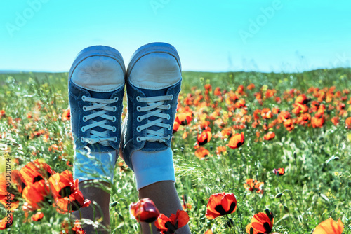 Legs of girls in sneakers in a poppy field. Concept of joy and happy childhood.