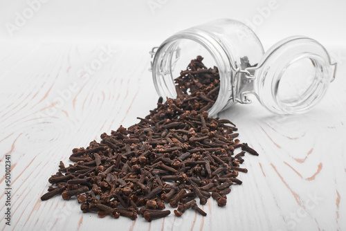 clove spice scattered from a jar on a white wooden background