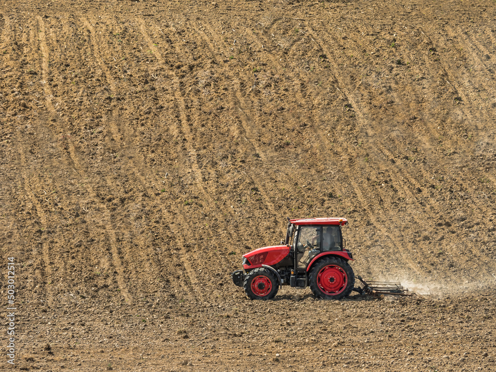Obraz premium Farm tractor harrowing arable field