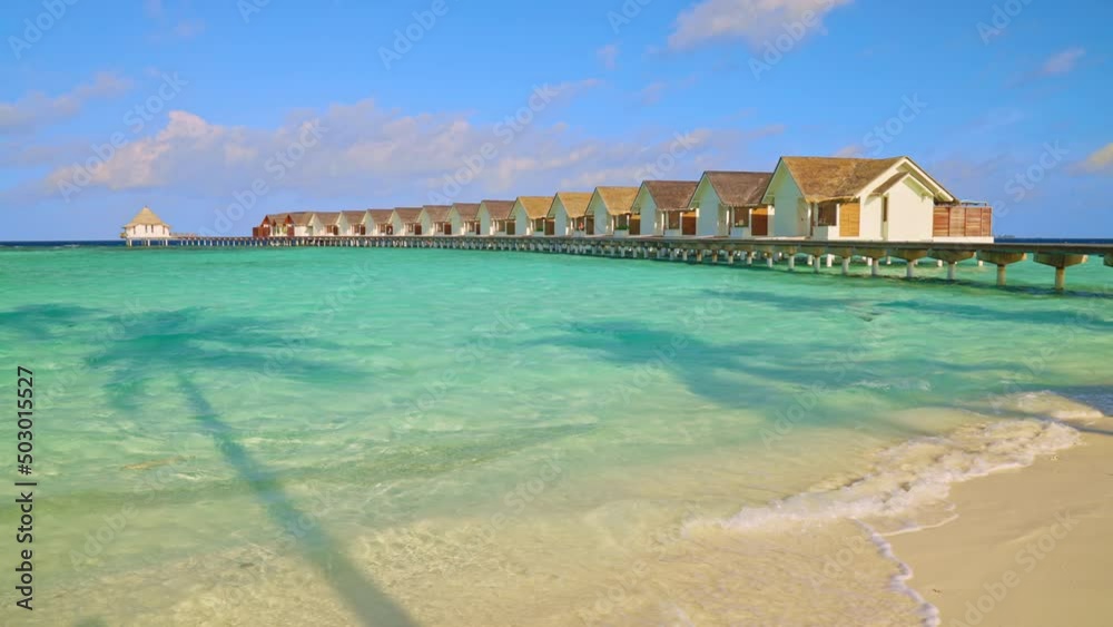 Sandy beach on a tropical Maldives island leading to luxury overwater bungalows