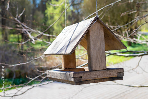 Bird feeder in the form of a house hanging on a tree. Park sunny summer day. Close-up of a small wooden birdhouse.