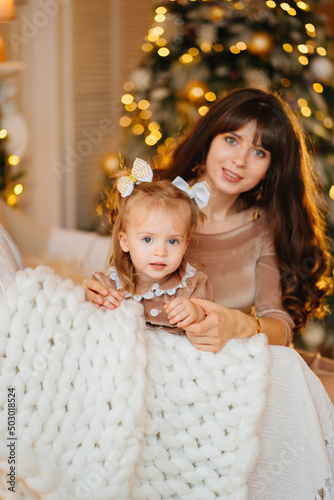 cute mother and daughter on a chair in a room with Christmas garlands. 