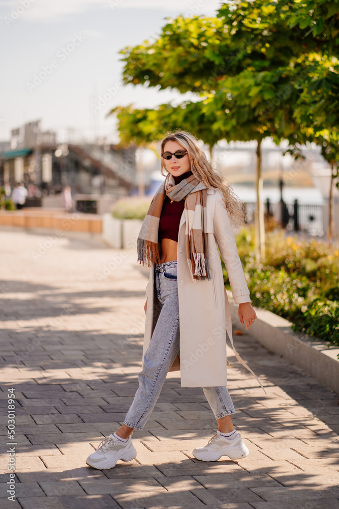 blonde student or businesswoman in a coat with scarf walks down an autumn street
