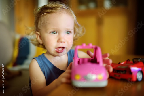 Cute toddler boy playing with colourful toy cars at home.