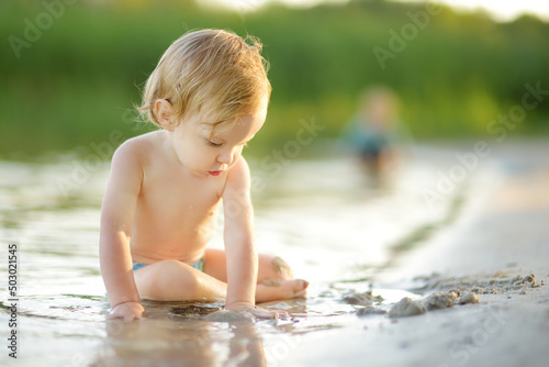 Cute toddler boy wearing swimming diaper playing by a river on hot summer day. Adorable child having fun outdoors during summer vacations.