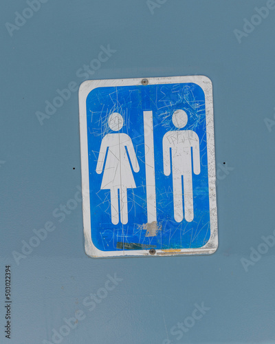 Close up of an old unisex bathroom sign on a door.