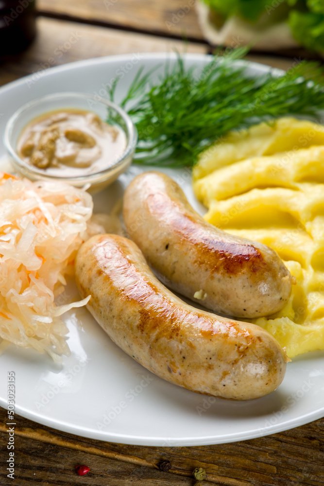 bavarian sausages with mashed potatoes and mustard on white plate on wooden table macro close up