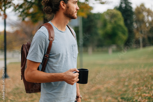 man wearing backpack standing outside with a cup of coffee photo