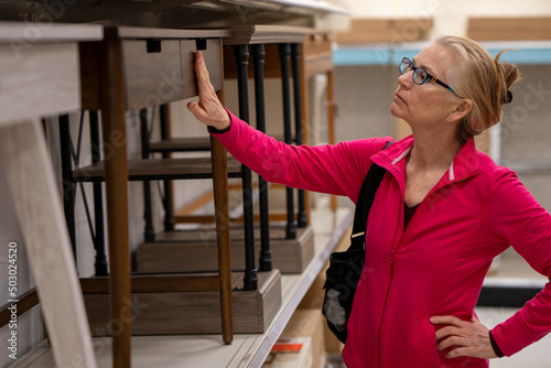 Closeup of pretty, blonde, mature woman inspecting the desks and quality of furniture in a store display.