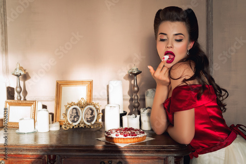 Pretty pin-up girl eats cake in retro interior. Temptation concept