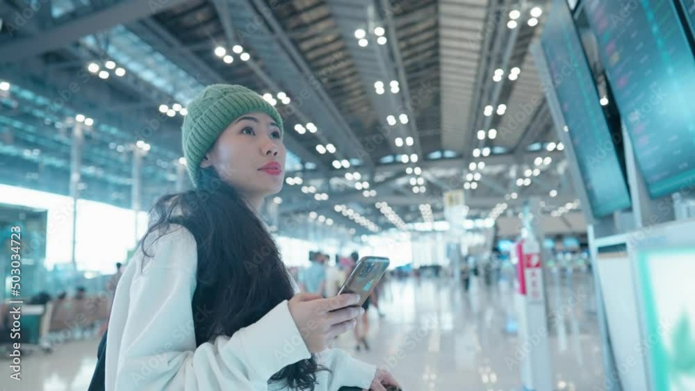 Asian tourist scanning on LED board flight information with looking on smartphone screen. Convenience Self Check-In Service Technology. Airline customer doing online registration at airport terminal Asian tourist scanning on LED board flight information with looking on smartphone screen. Convenience Self Check-In Service Technology. Airline customer doing online registration at airport terminal