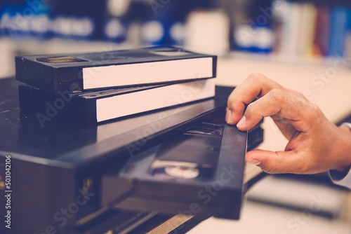 Photos Close-up hand put or insert video cassette tape VHS old retro style on video record playback concept of vintage electric and electronic appliances multimedia player device old fashioned