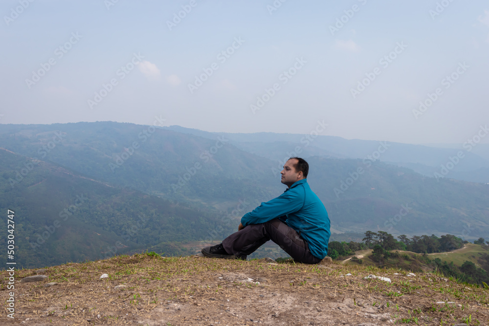 man sitting alone at hill top with misty mountain rage background from flat angle