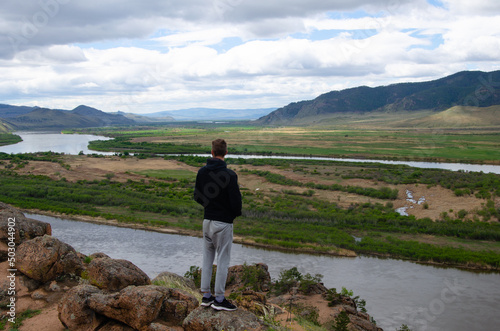 A man stands high on a hill and looks into the distance. Below is the river and the mountains.