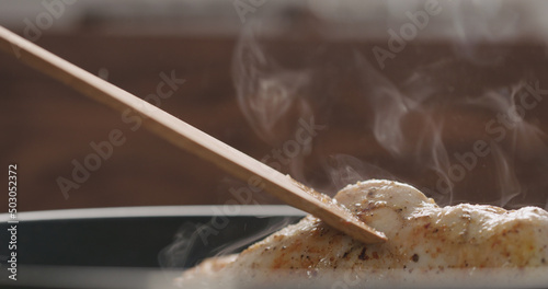 man hand moving chicken fillet in pan with wood spatula closeup