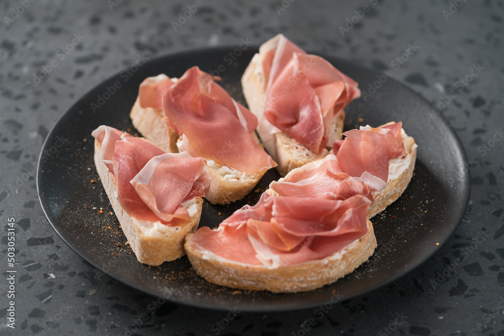 bruschetta with prosciutto and cream cheese on black plate on conctere background