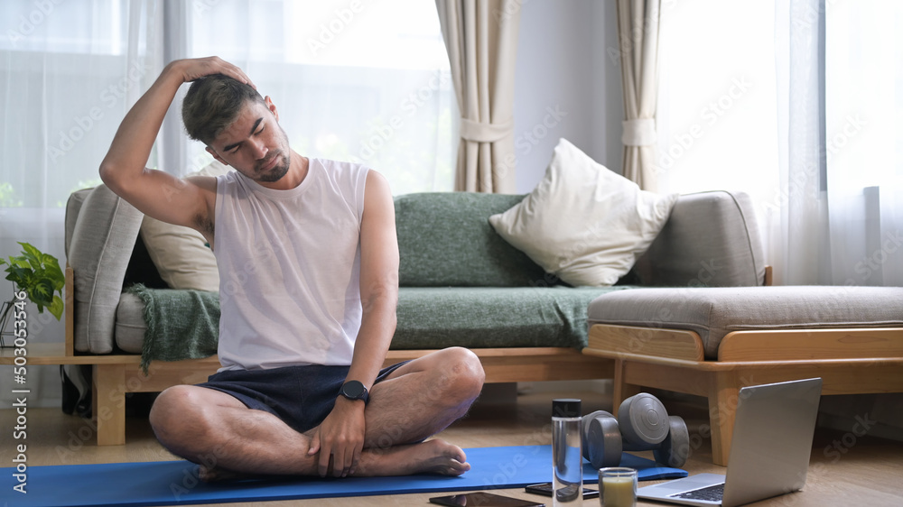 Millennial man exercising at home and watching fitness lessons online on laptop.