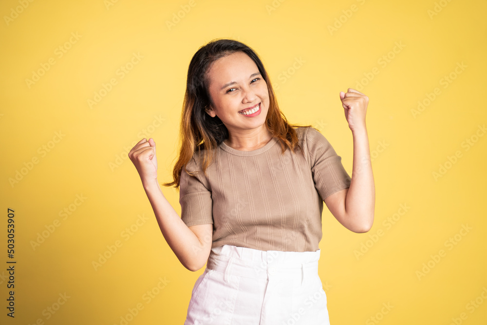 Excited young asian woman clenching hands while celebrating success on isolated background Excited young asian woman clenching hands while celebrating success on isolated background