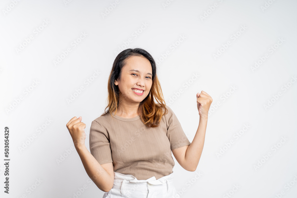 Excited young asian woman clenching hands while celebrating success on isolated background Excited young asian woman clenching hands while celebrating success on isolated background
