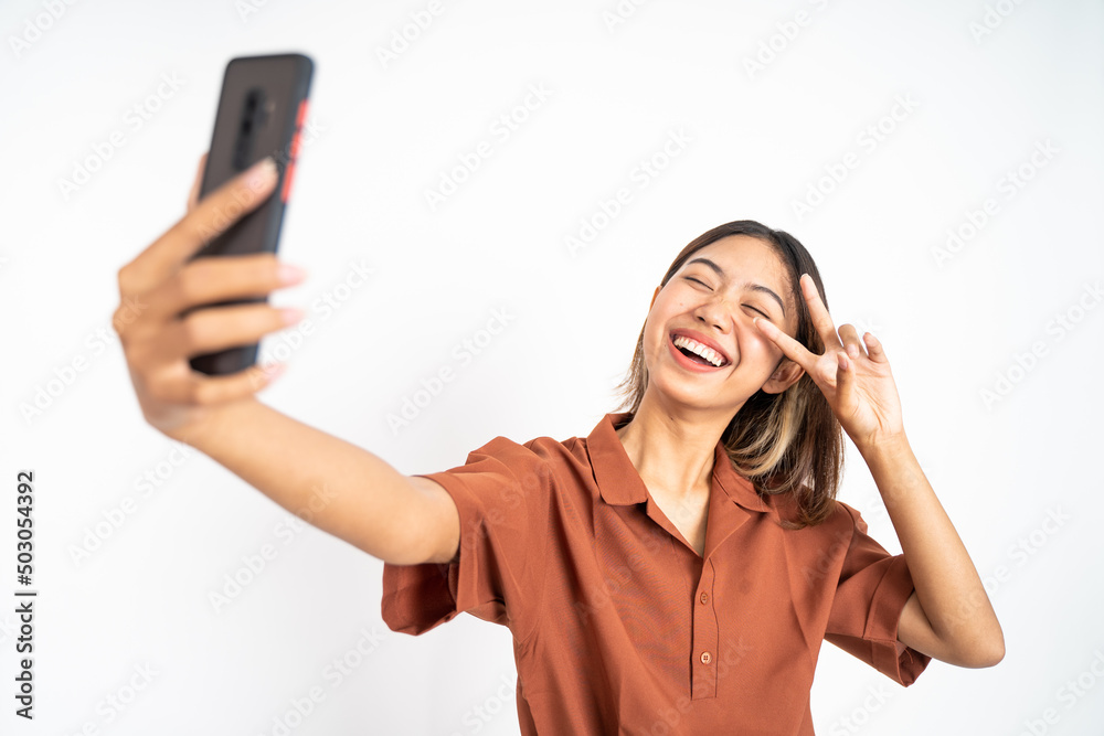 attractive woman take a selfie using mobile phone camera with v sign finger gesture on isolated background attractive woman take a selfie using mobile phone camera with v sign finger gesture on isolated background