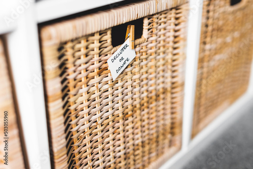 decluttering and tidying up concept, basket with Declutter or Donate label on it with unfocused storage cabinet and other baskets in the background