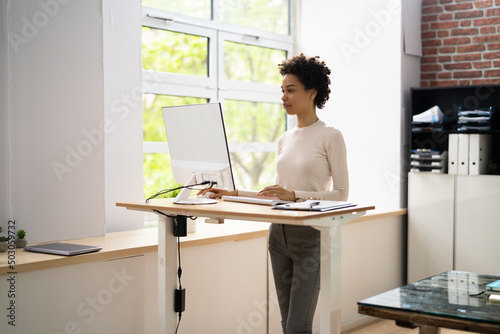 Woman Using Adjustable Height Standing Desk In Office