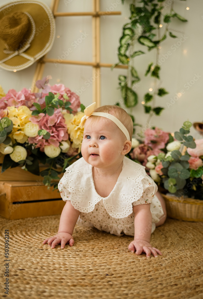 a beautiful baby girl in a colored bodysuit with a headband crawls on the carpet among flower boxes a beautiful baby girl in a colored bodysuit with a headband crawls on the carpet among flower boxes