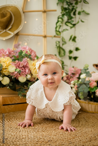 a smiling baby girl in a colored bodysuit with a headband crawls on the carpet among flower boxes