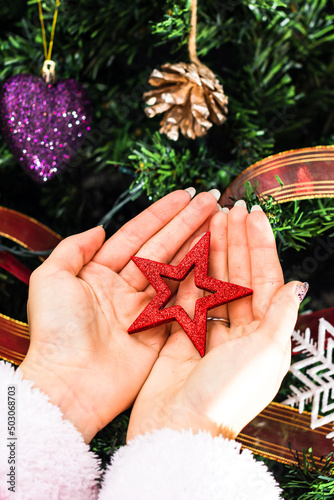 Vertical closeup of female hands holding a Christmas cdecoration in front of a fir tree photo