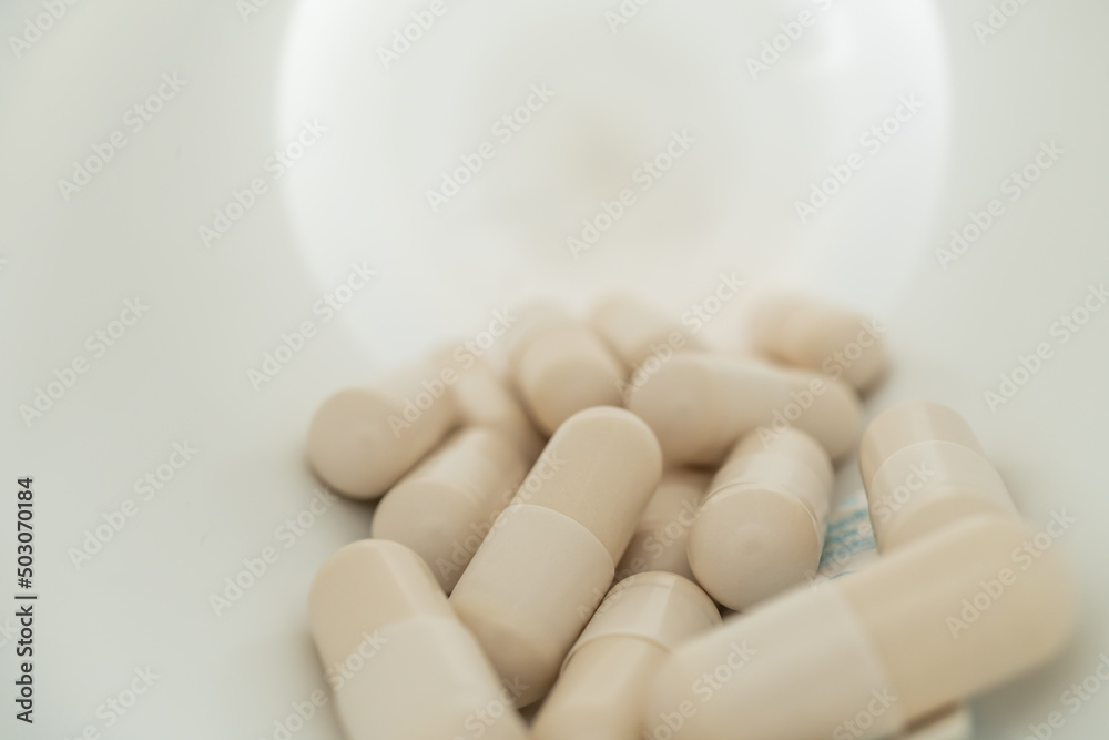 White capsules inside opened supplement plastic bottle. Several white capsules in the white bottle. White capsules inside opened supplement plastic bottle. Several white capsules in the white bottle.