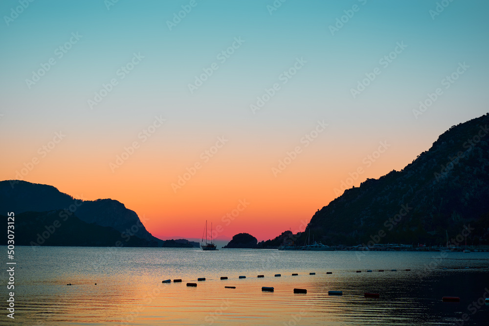 Beautiful sunrise with yacht sailing the sea with rocks islands on the background.