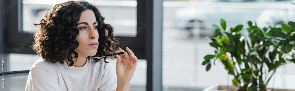 Obraz premium Thoughtful arabian businesswoman holding pen in office, banner.