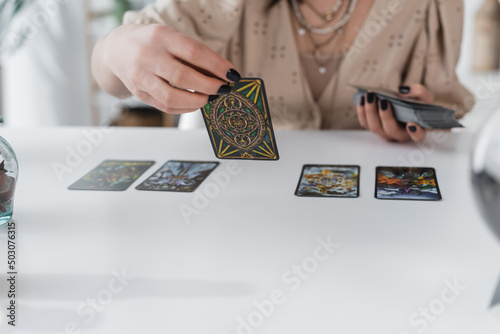 KYIV, UKRAINE - FEBRUARY 23, 2022: Cropped view of blurred medium holding tarot cards at home.