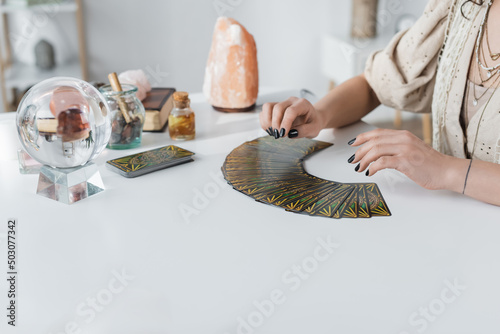 KYIV, UKRAINE - FEBRUARY 23, 2022: Cropped view of medium near tarot cards and witchcraft supplies on table. photo