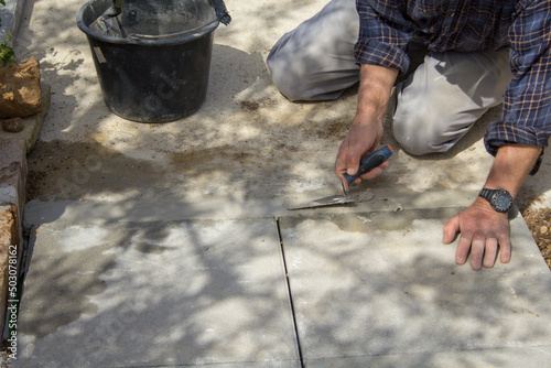 Image of the hands of an elderly bricklayer who, with a trowel and concrete, builds a path in the backyard. 