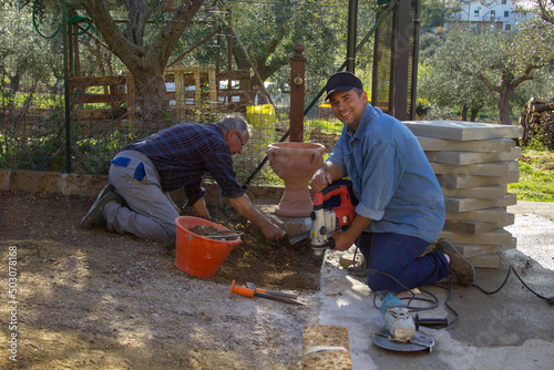 Wallpaper Mural 
Image of a young man and an elderly bricklayer building a driveway in their backyard using a trowel, concrete and demolition hammer. Torontodigital.ca