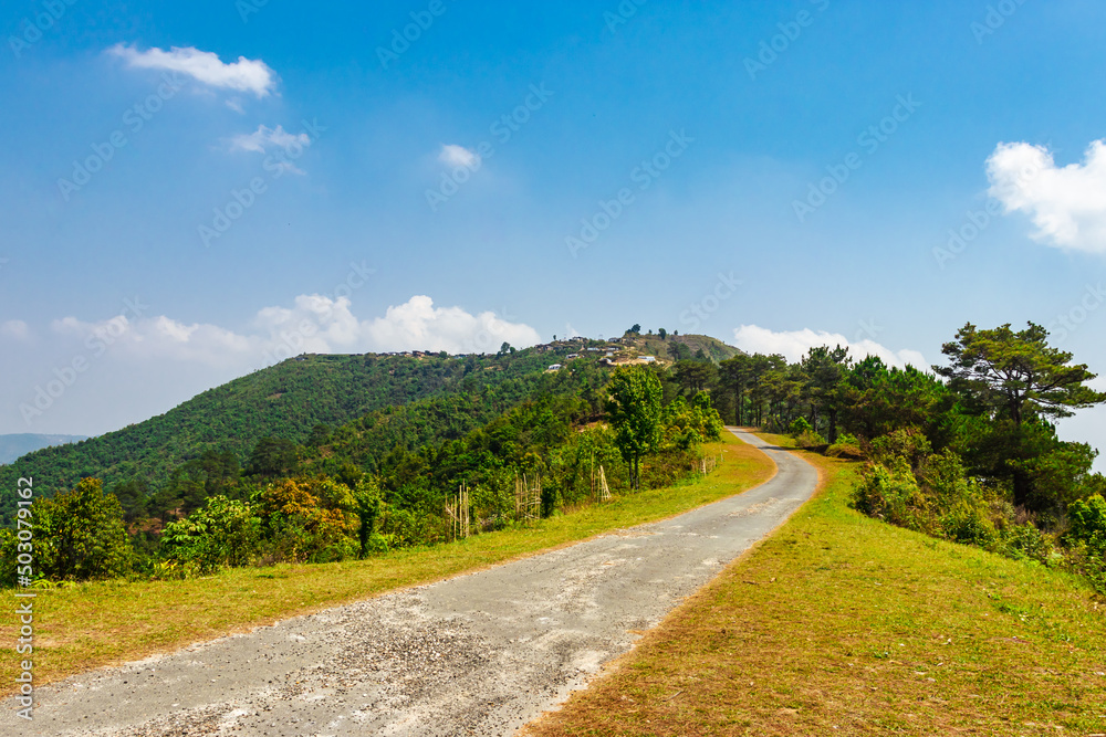 isolated road with mountain covered with green forests and bright blue sky at morning