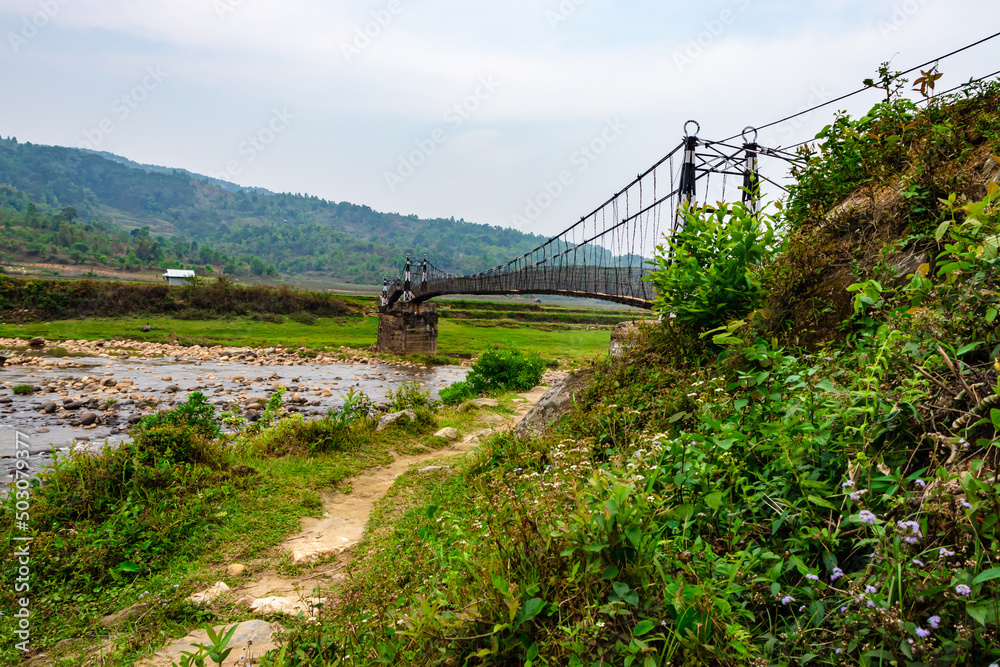 Fototapeta premium isolated iron suspension bridge over flowing river with misty mountain background at morning