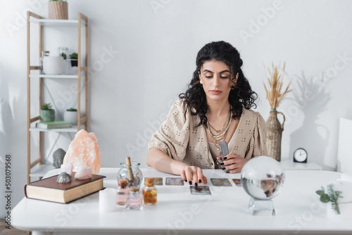 Gypsy fortune teller holding tarot cards near blurred orb on table.