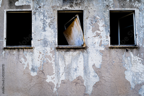stary opuszczony budynek z rozbitymi oknami i zdartą farbą ze ściany