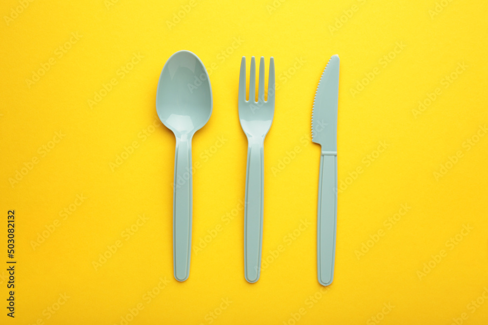 Blue plasic forks, spoons and knives on yellow background with copy space, top view. Blue plasic forks, spoons and knives on yellow background with copy space, top view.