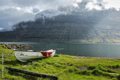 Rowboat moored on the grassy shore in Eskifjörður fjord, Iceland. cloud-covered Hólmatindur mountain in the background photo