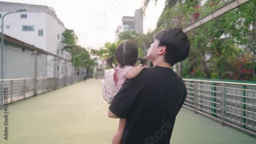 Back to School. Asian young father holding a little schoolgirl walking along urban green pedestrian bridge. School Education System. Childhood early age caring. Happy family goes to school together. 