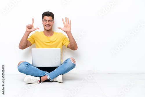 Young man sitting on the floor isolated on white background counting seven with fingers