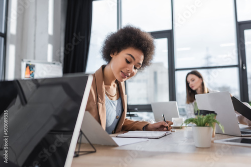 Smiling african american businesswoman looking at notebook in office.