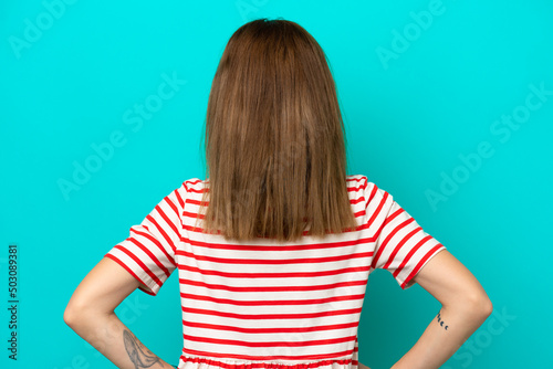 Young English woman isolated on blue background in back position