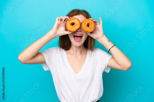 Young English woman isolated on blue background holding donuts in an eye